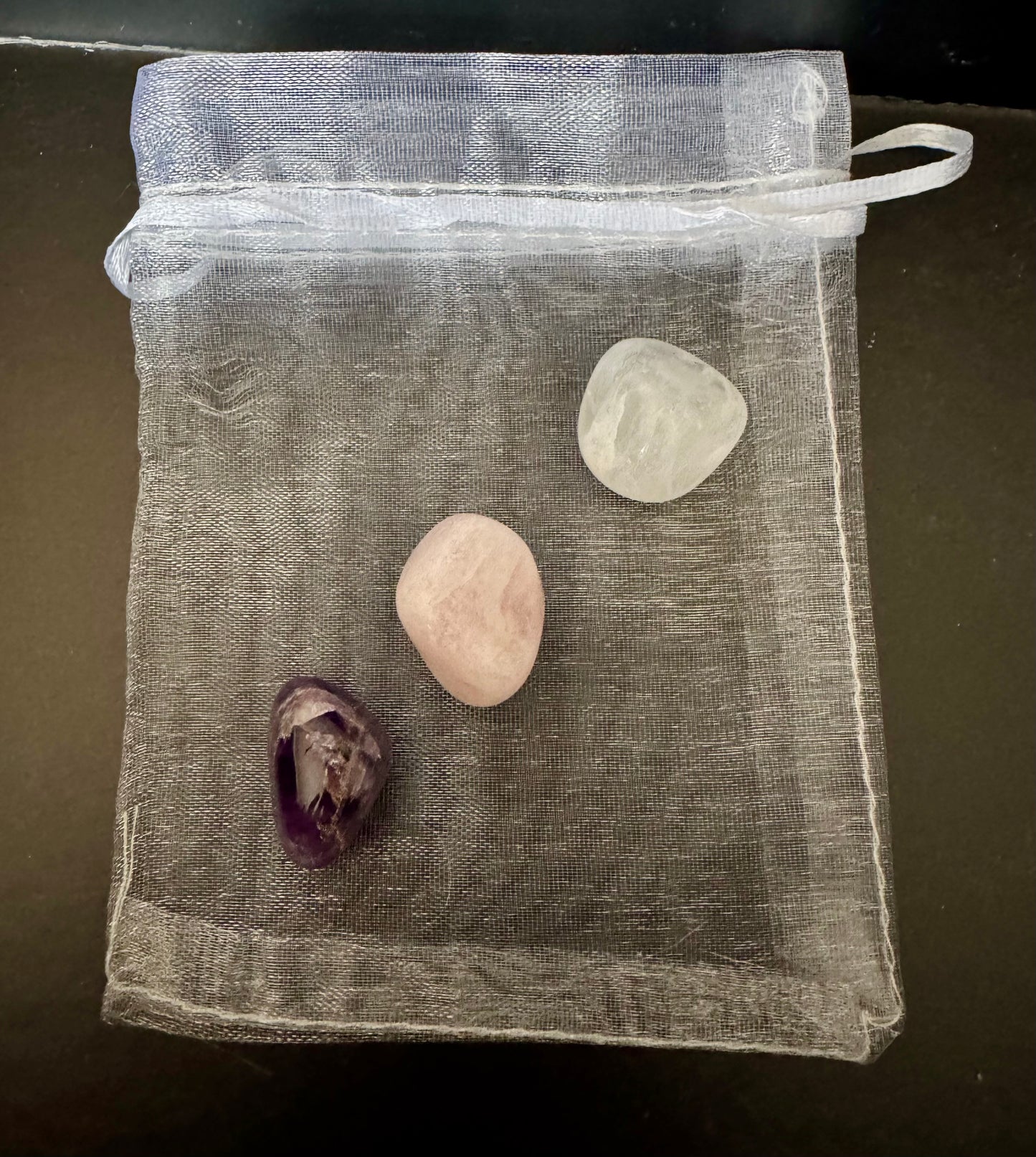 Three stones inside a clear drawstring bag on a dark surface