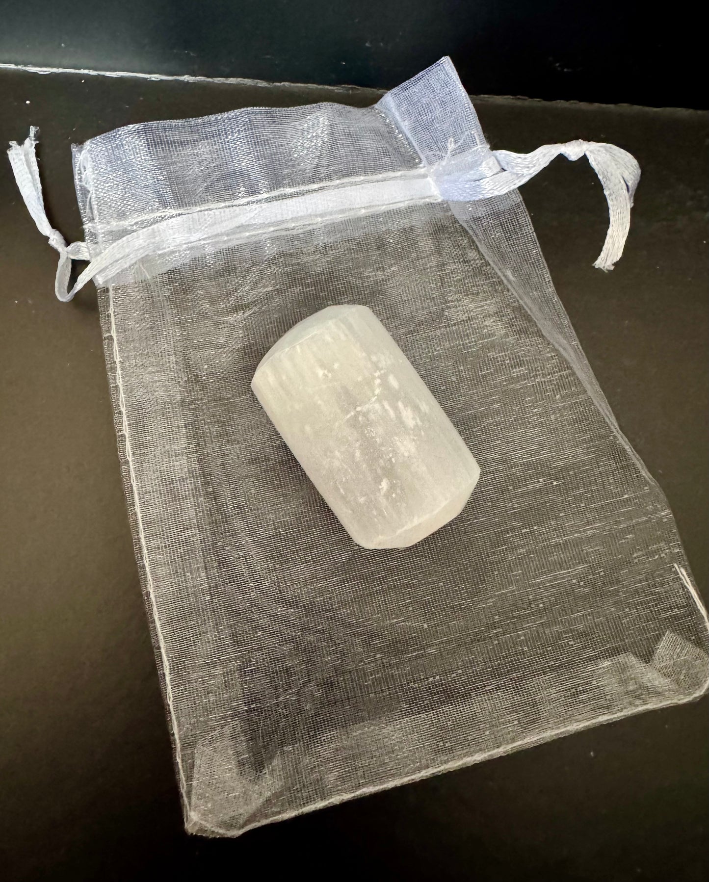 Selenite on a clear drawstring bag on a dark surface