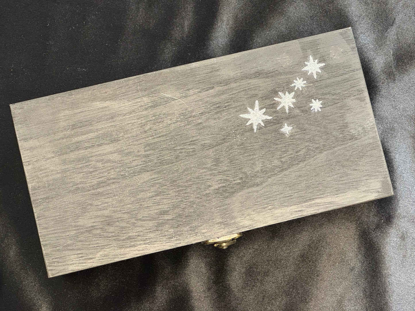 A rectangular black wooden box with a small gold clasp and white star detail.