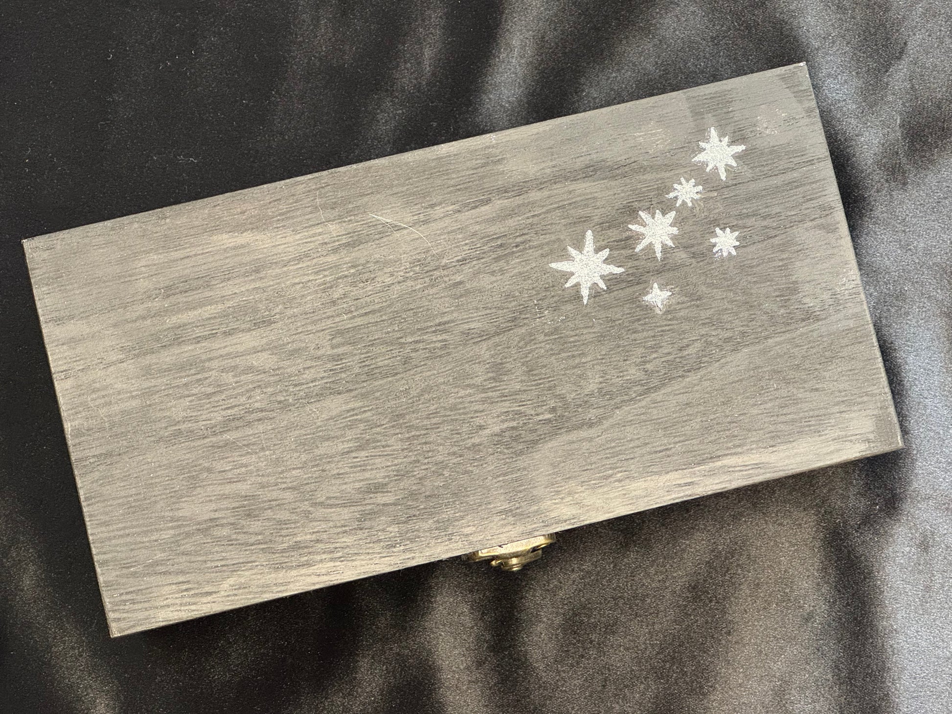 A rectangular black wooden box with a small gold clasp and white star detail.