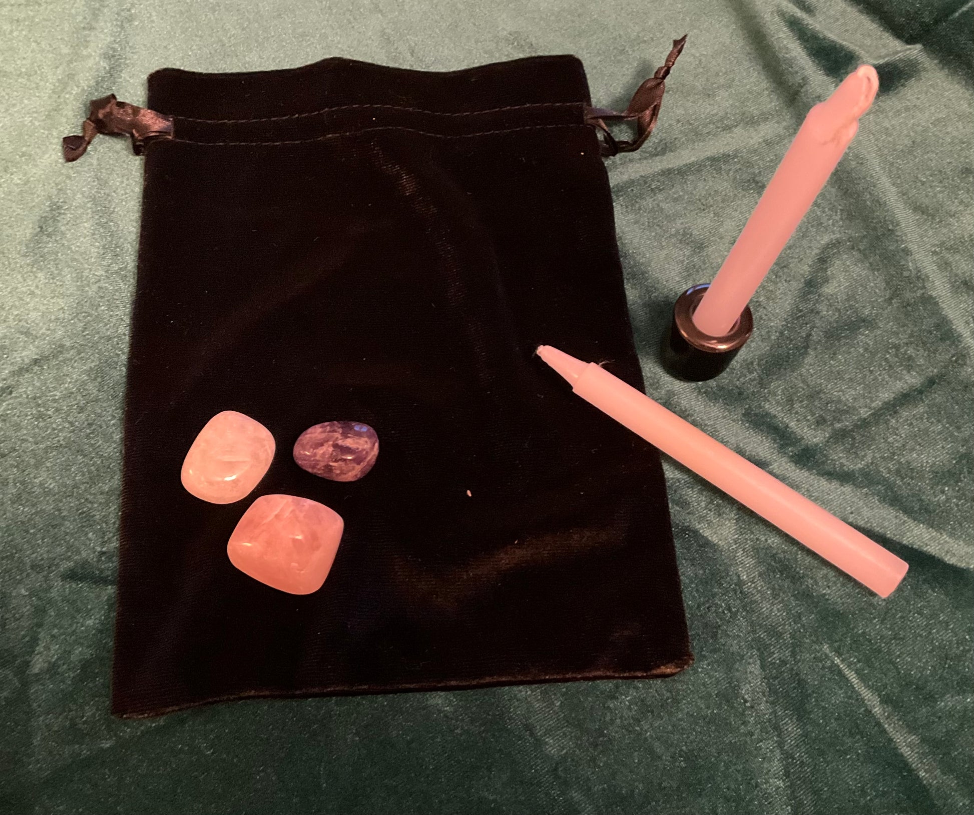 Black velvet drawstring bag with pink stones and candles on a green fabric background